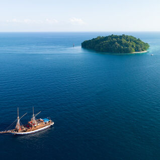 Aerial view of a tropical island, surrounded by coral reef with a liveaboard sailing boat