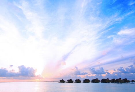 Sunset over the waters with thatched roof villas