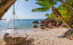 view of the beach with blue water, green jungle and a hammock