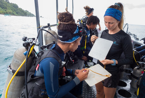 Two women on a diving boat. one is wearing diving kit and tank the other is showing her the dive plan.
