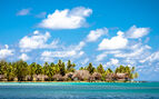 Traditional Polynesian bungalows sitting along the water side in Huahine Island in Polynesia with palm trees