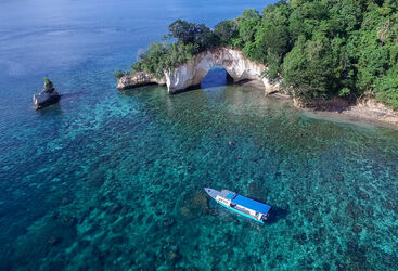 Aerial shot of a snorkelling boat in blue waters with white cliffs and lush jungle