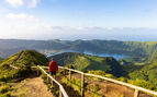 A hiker walking along a pathway in the Azores with green mountains and a lake in th background