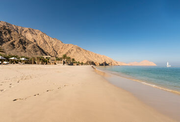 View of the beach in with rocky mountains on one side and the calm sea on the other at sunset.