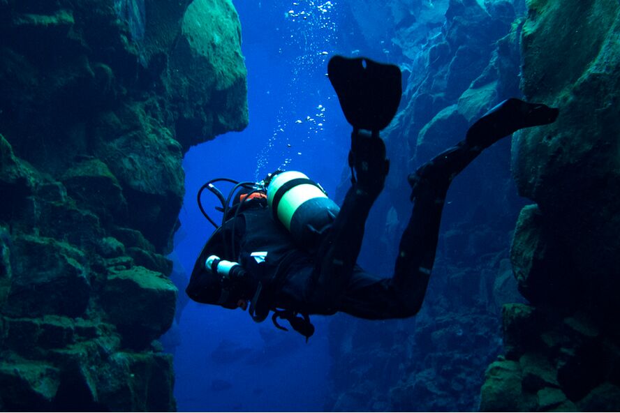underwater photo of a diver swimming in clear water between two walls