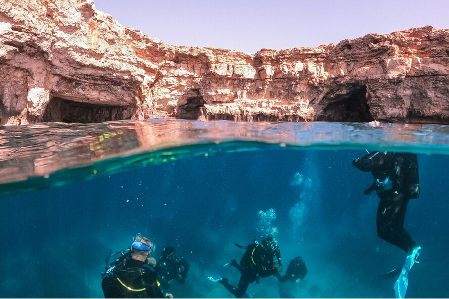 split view photo of divers in clear water with rocky cliffs surrounding them