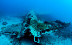 underwater photo of a plane wreck with patches of coral resting in blue water