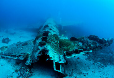 Undewater photo of a plane wreck with patches of coral in blue waters