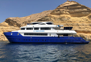 A side, water level photo of a liveaboard floated on water with yellow rock formations in the background
