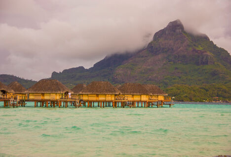 Huts on the water with sunset in the background in Tahiti
