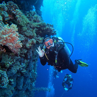Underwater photo of a scuba diver giving the 'OK' sign next to a coral reef wall